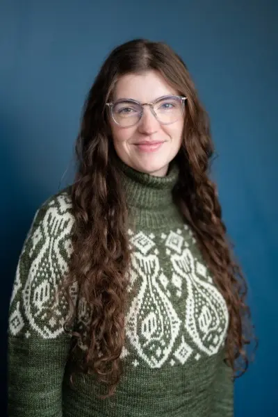 Giulia Wood in green sweater standing in front of blue background.