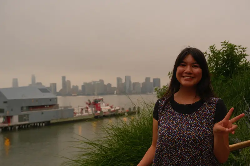 CJ Chavez poses with a peace sign in front of a cityscape.